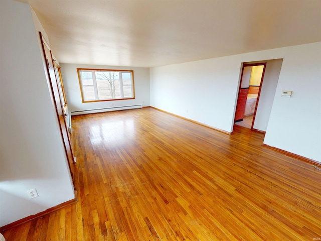 empty room featuring a baseboard heating unit, light wood finished floors, and baseboards