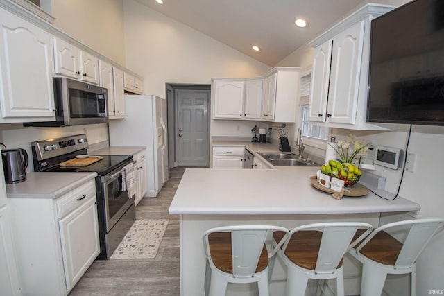 kitchen with appliances with stainless steel finishes, a peninsula, vaulted ceiling, white cabinetry, and a sink