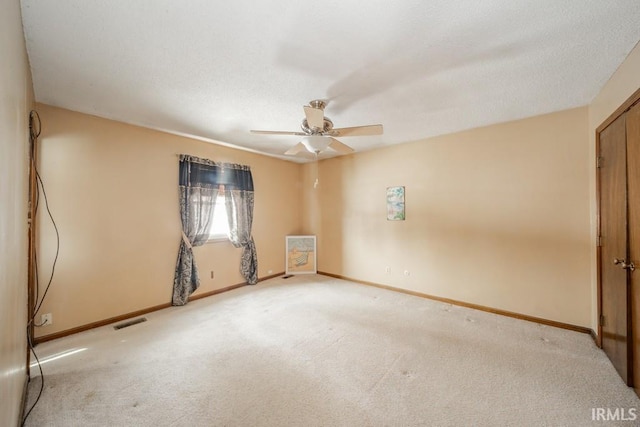 carpeted spare room featuring visible vents, ceiling fan, and baseboards