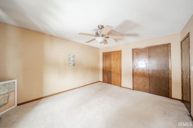 unfurnished bedroom with two closets, carpet flooring, ceiling fan, a textured ceiling, and baseboards