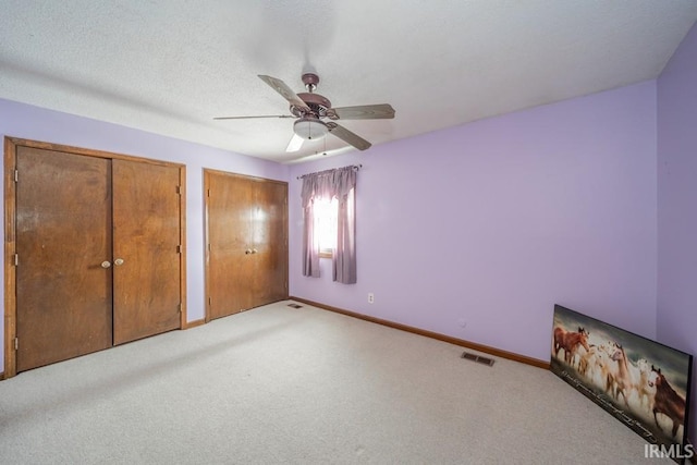 unfurnished bedroom featuring baseboards, a textured ceiling, visible vents, and two closets