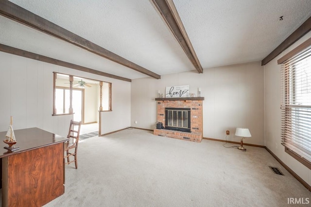 carpeted living area with plenty of natural light, visible vents, a textured ceiling, a brick fireplace, and beam ceiling