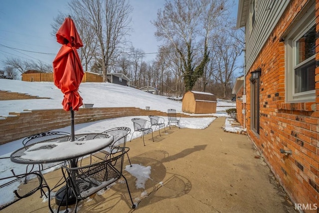 snow covered patio featuring an outbuilding, a shed, and fence