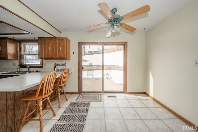 kitchen with baseboards, a breakfast bar, brown cabinets, a peninsula, and light countertops