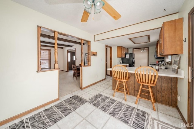 kitchen with ceiling fan, baseboards, light countertops, freestanding refrigerator, and brown cabinetry