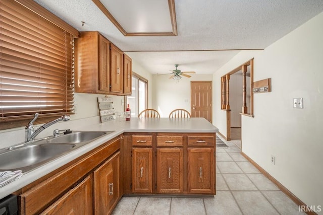 kitchen featuring light countertops, brown cabinets, a sink, and a peninsula