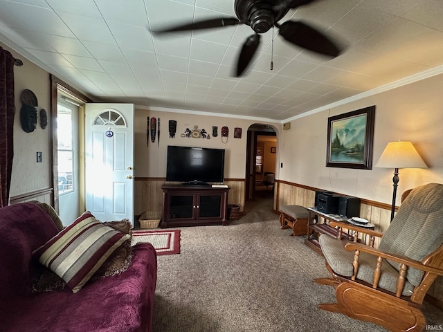 carpeted living room featuring wood walls, arched walkways, ornamental molding, and wainscoting