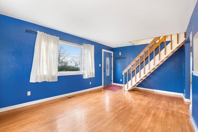 unfurnished living room with hardwood / wood-style flooring, baseboards, stairs, and visible vents