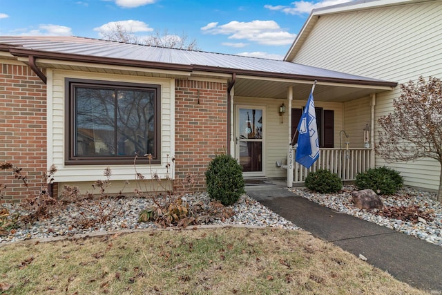 entrance to property featuring covered porch, brick siding, and metal roof