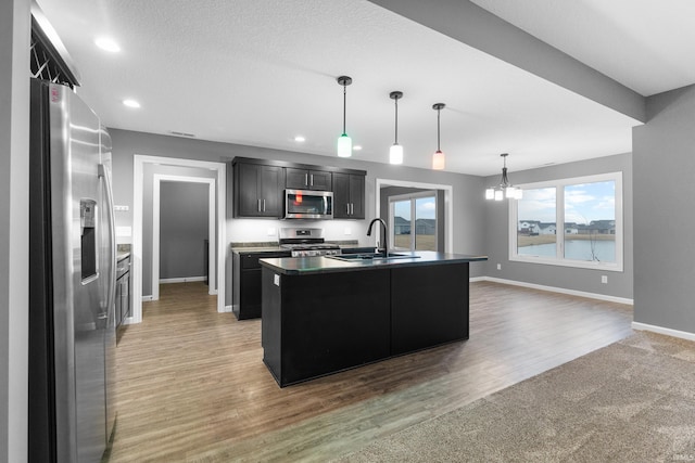 kitchen with a sink, light wood-style floors, baseboards, appliances with stainless steel finishes, and dark countertops