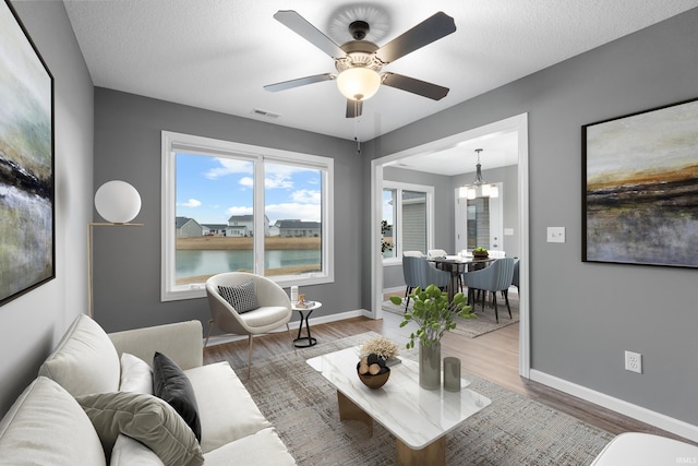 living room featuring ceiling fan with notable chandelier, wood finished floors, visible vents, and baseboards