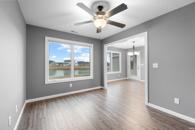 empty room with ceiling fan with notable chandelier, wood finished floors, visible vents, and baseboards