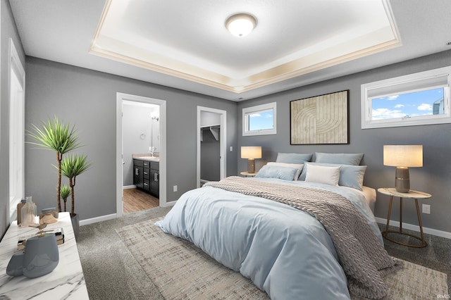 bedroom featuring a tray ceiling, a sink, connected bathroom, and baseboards