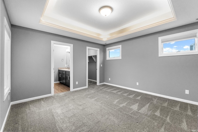 unfurnished bedroom with carpet floors, a tray ceiling, and baseboards