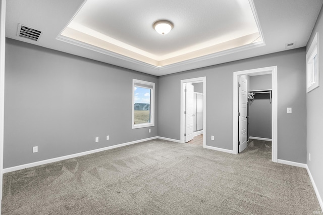 unfurnished bedroom with carpet floors, visible vents, baseboards, a spacious closet, and a tray ceiling