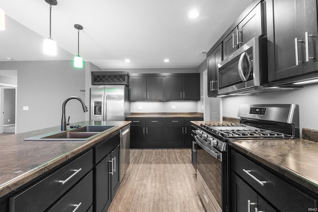 kitchen featuring decorative light fixtures, light wood finished floors, dark countertops, appliances with stainless steel finishes, and a sink