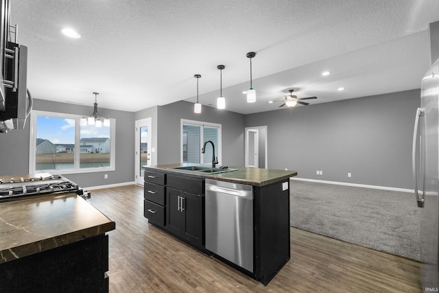 kitchen with dark countertops, appliances with stainless steel finishes, open floor plan, dark cabinetry, and a sink