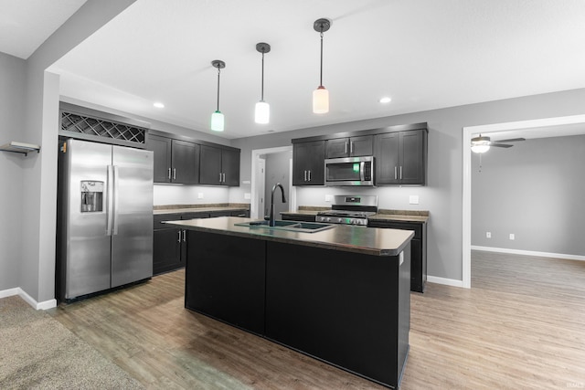 kitchen with dark countertops, appliances with stainless steel finishes, light wood-style floors, a sink, and ceiling fan