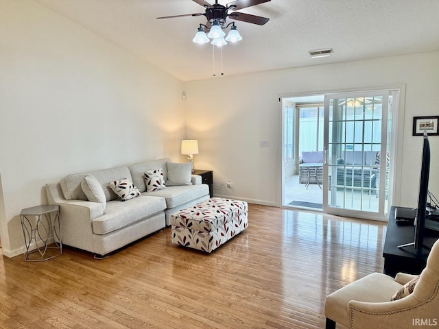 living room with baseboards, visible vents, ceiling fan, and light wood finished floors