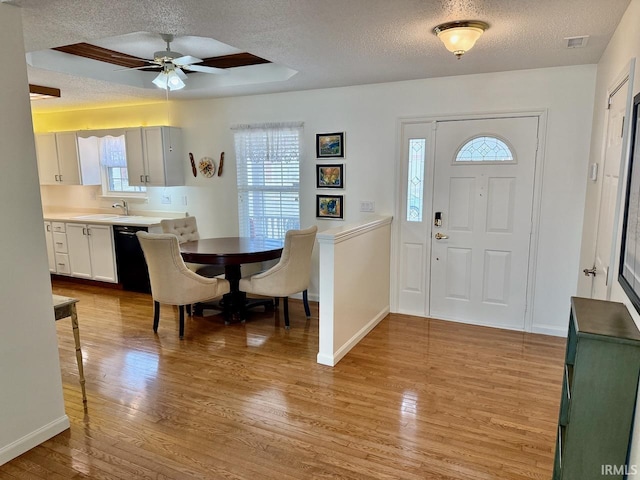 foyer featuring light wood-style floors, visible vents, a tray ceiling, and a textured ceiling