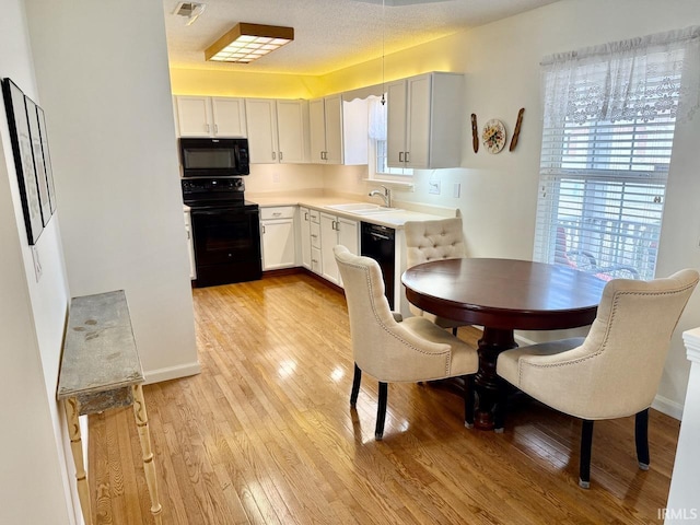 kitchen featuring light countertops, visible vents, light wood-style floors, a sink, and black appliances