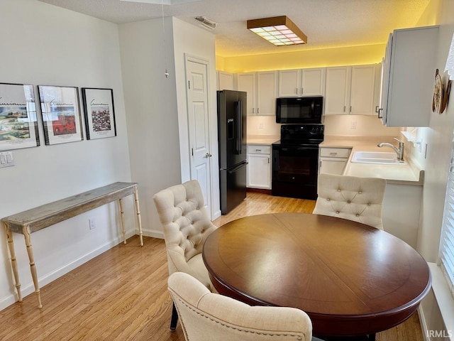 kitchen featuring a sink, visible vents, light wood-style floors, light countertops, and black appliances