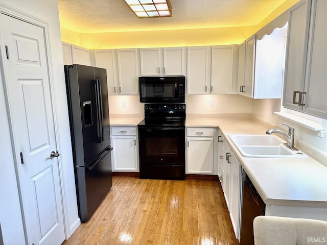 kitchen featuring a textured ceiling, black appliances, a sink, and light wood-style floors