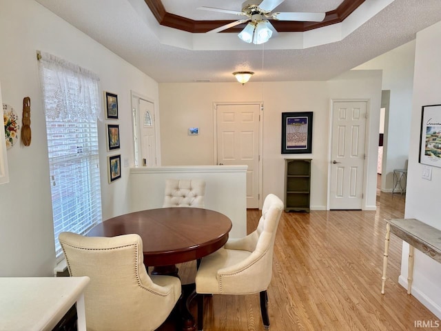 dining space featuring baseboards, a raised ceiling, a ceiling fan, crown molding, and light wood-type flooring