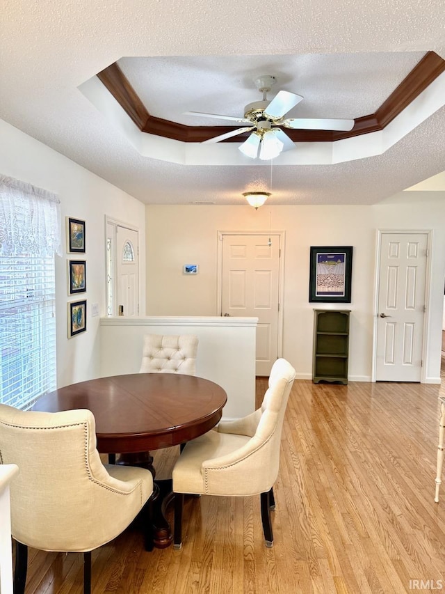 dining space featuring a textured ceiling, ornamental molding, light wood-type flooring, and a raised ceiling