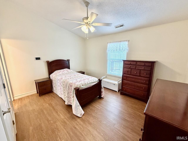 bedroom with light wood finished floors, visible vents, ceiling fan, a textured ceiling, and baseboards