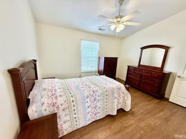 bedroom with a ceiling fan, a textured ceiling, visible vents, and wood finished floors