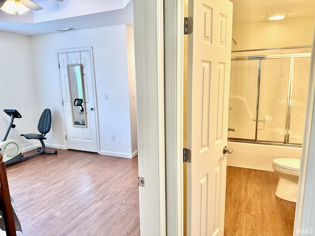 interior space featuring bath / shower combo with glass door, toilet, a ceiling fan, wood finished floors, and baseboards