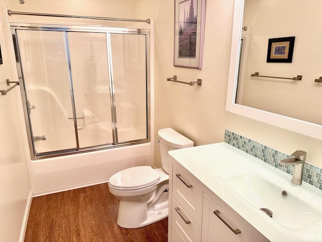 bathroom featuring decorative backsplash, toilet, enclosed tub / shower combo, wood finished floors, and vanity