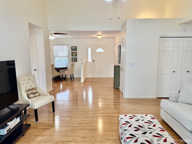 living area featuring a towering ceiling, light wood finished floors, baseboards, and a ceiling fan