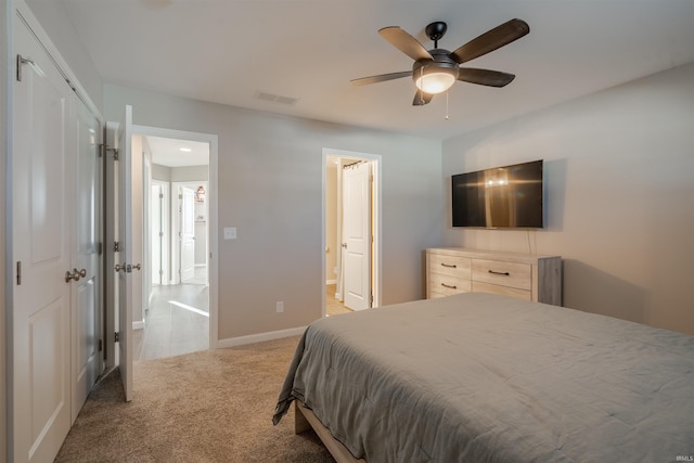 bedroom featuring light colored carpet, a ceiling fan, baseboards, visible vents, and ensuite bath