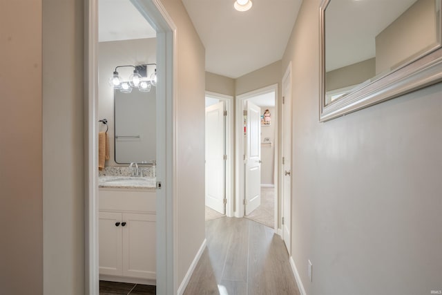 corridor with a sink, baseboards, and wood finished floors