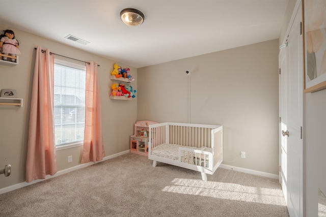 unfurnished bedroom with carpet, visible vents, a crib, and baseboards