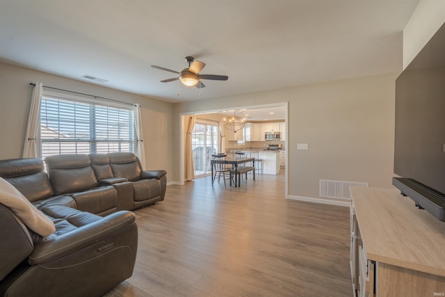 living room featuring ceiling fan with notable chandelier, visible vents, baseboards, and wood finished floors