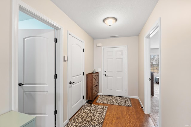 doorway to outside featuring baseboards, a textured ceiling, visible vents, and wood finished floors