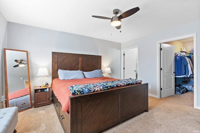 bedroom featuring a walk in closet, light carpet, ceiling fan, and baseboards