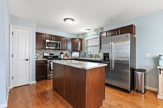 kitchen with light wood-type flooring, dark brown cabinetry, appliances with stainless steel finishes, and backsplash