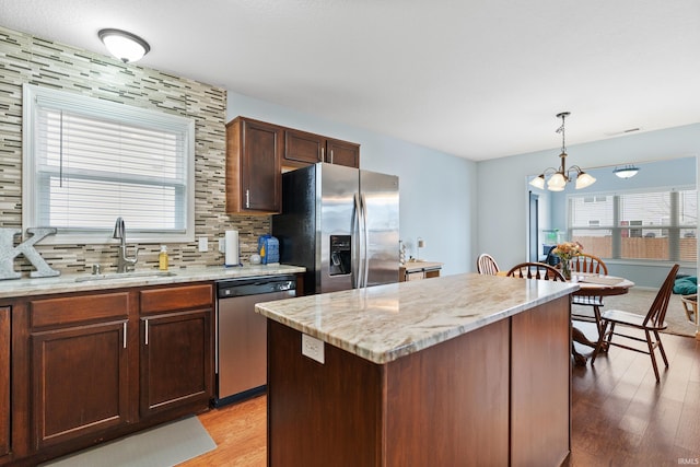 kitchen featuring a center island, light wood-style flooring, decorative backsplash, appliances with stainless steel finishes, and a sink