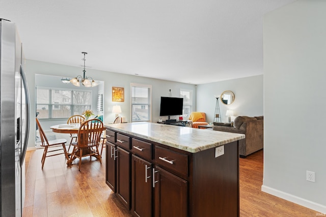 kitchen featuring pendant lighting, light wood-style flooring, dark brown cabinetry, light stone countertops, and stainless steel fridge