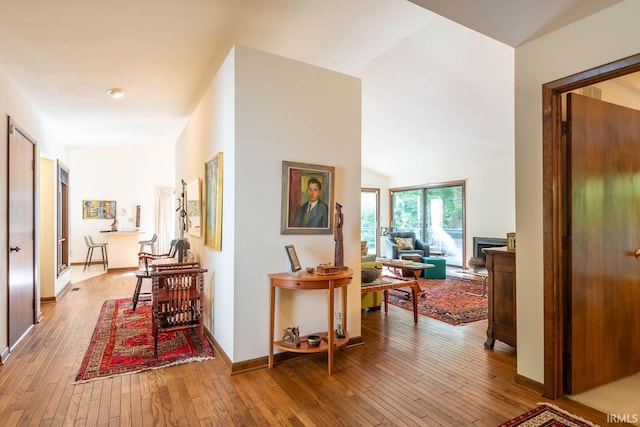 hall featuring vaulted ceiling, wood-type flooring, and baseboards