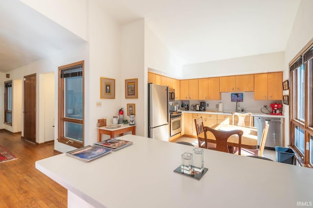 kitchen featuring hardwood / wood-style floors, stainless steel appliances, light countertops, light brown cabinetry, and high vaulted ceiling