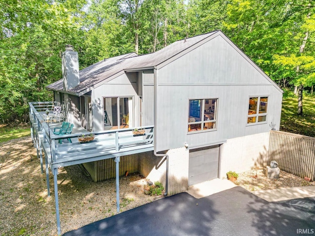 view of front of house with aphalt driveway, a wooden deck, a chimney, and an attached garage