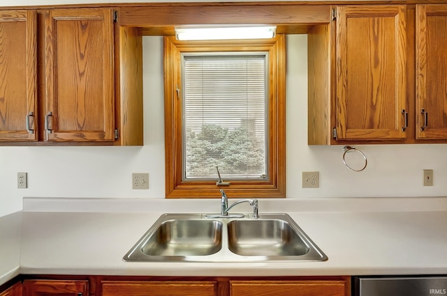 kitchen with light countertops, stainless steel dishwasher, a sink, and brown cabinets