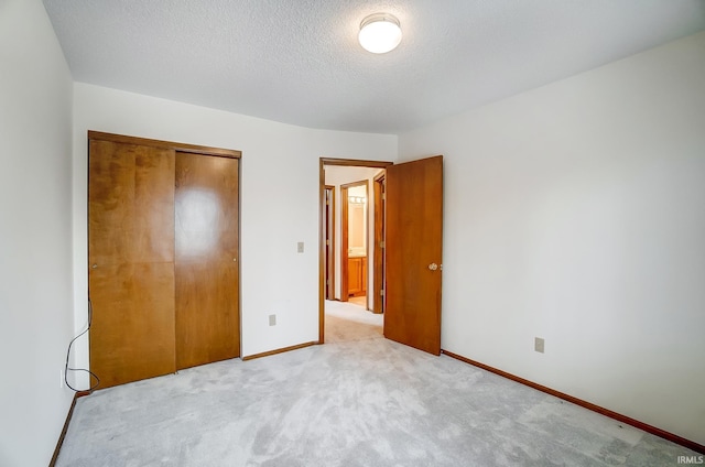 unfurnished bedroom with carpet floors, a textured ceiling, baseboards, and a closet