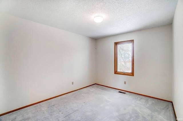 spare room featuring a textured ceiling, carpet floors, visible vents, and baseboards