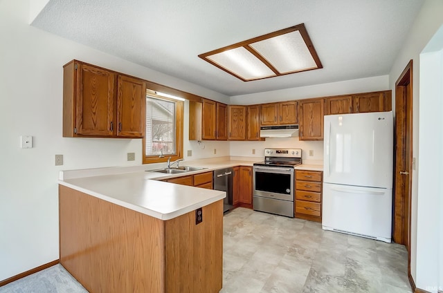 kitchen with appliances with stainless steel finishes, brown cabinets, a peninsula, light countertops, and a sink